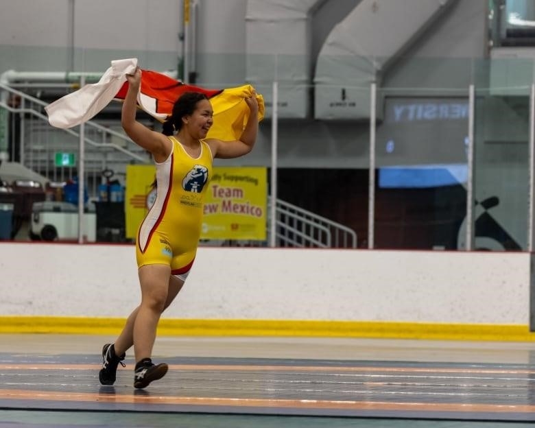 A girl runs, holding a flag high in the air and grinning.