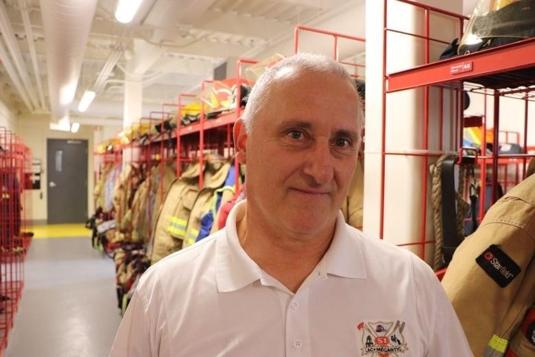 A man stands in front of a row of firefighter uniforms 
