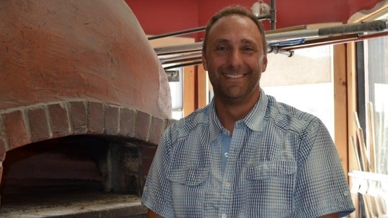 Derek Lucchese standing in front of a brick wood-fire oven in his restaurant.