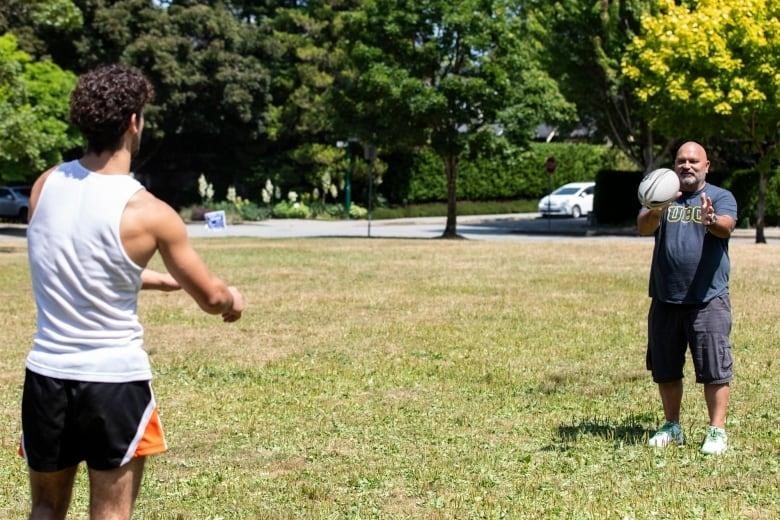 A young man throws a rugby ball to a man in his fifties