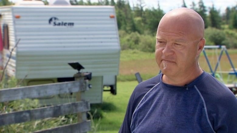 A man stands in a field beside a camper trailer
