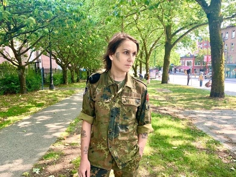 A woman wears a camouflaged suit in a park.