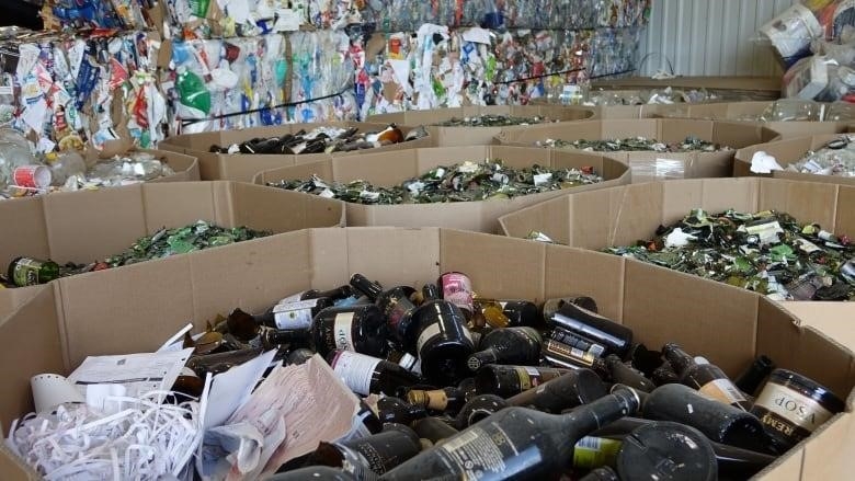 Bins filled with broken glass bottles and recycling packages behind them.