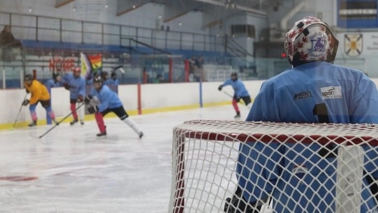 A hockey goalie watches players skate to their left.