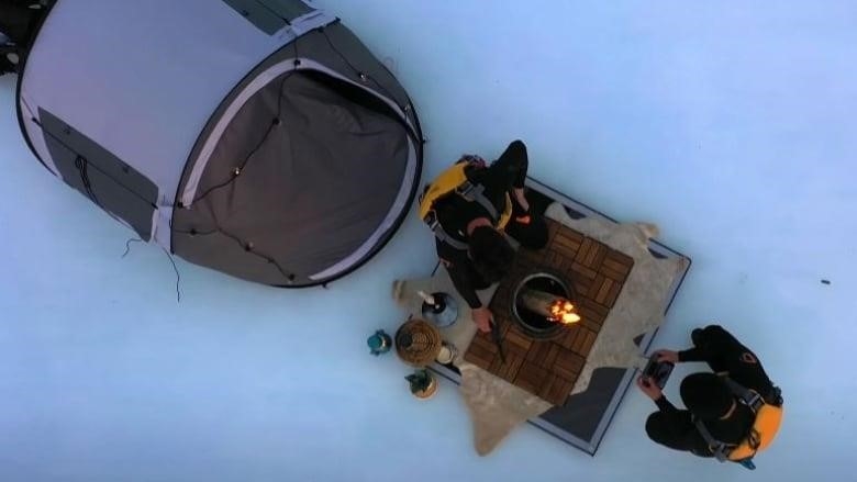 Two men sit near a campfire on top of a sheet of ice. 