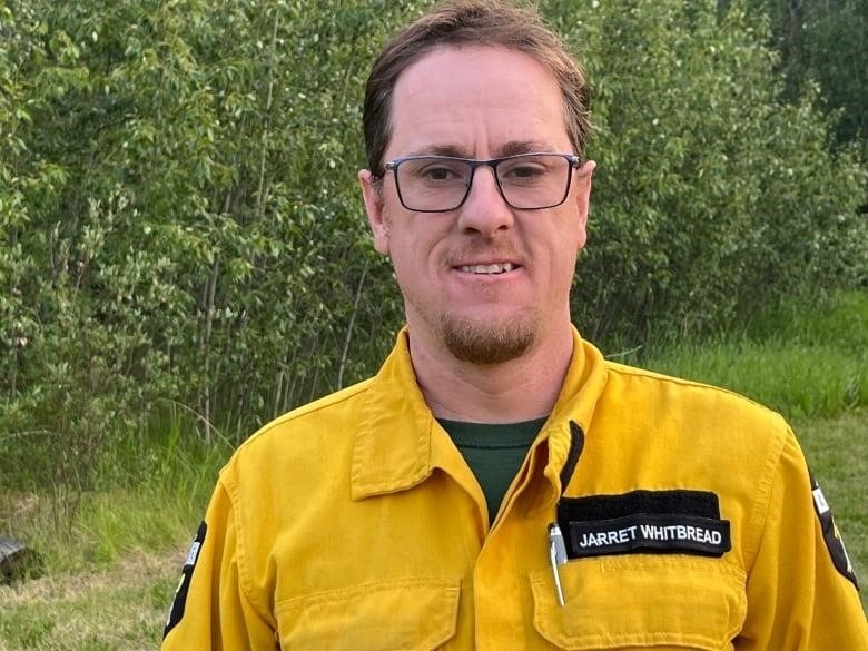 A man in a yellow uniform stands in front of trees.