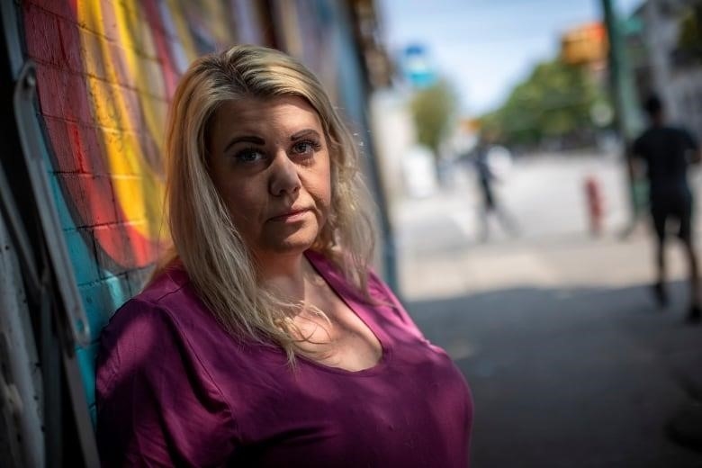 A blonde woman wears a purple shirt in front of a graffiti wall downtown Vancouver.