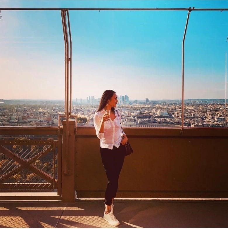 A girl in a white shirt and blue jeans with the skyline behind her