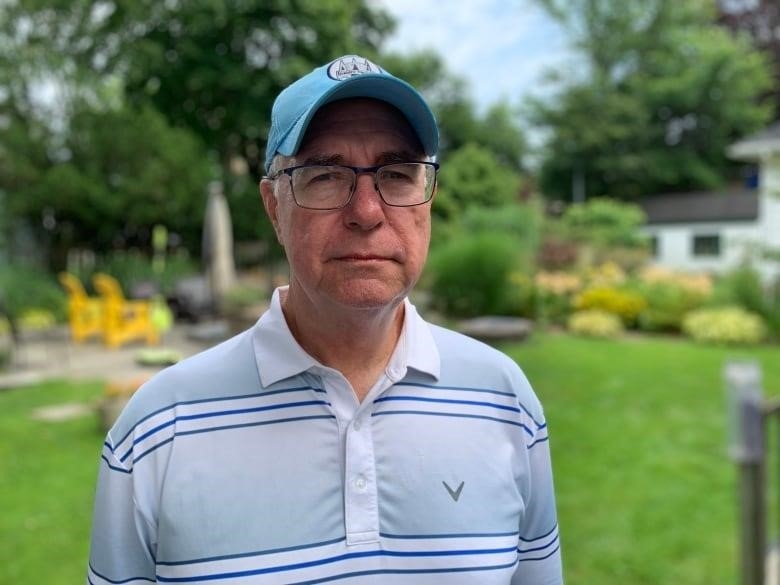 Jim Abraham, a former meteorologist with Environment and Climate Change Canada, poses for a picture. He is wearing a light blue striped golf shirt and a blue baseball cap. 