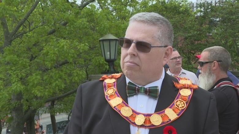 A man in a tuxedo with a special Royal Oak Orange Lodge necklace is pictured in front of some trees.