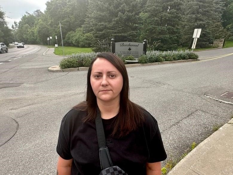 A woman with dark hair stands outside a graveyard 