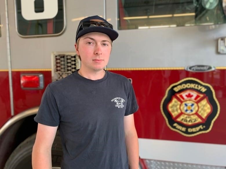 A young man stands in front of a fire truck.