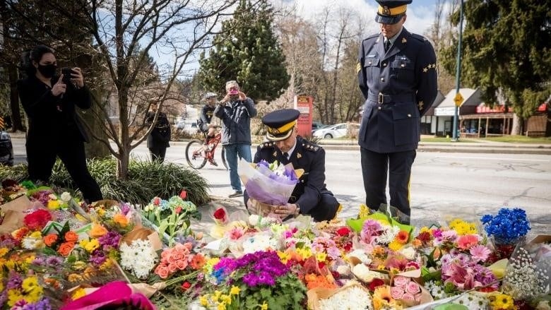 A uniformed RCMP officer kneels as he places a bouquet of flowers on a pile of similar bouquets.
