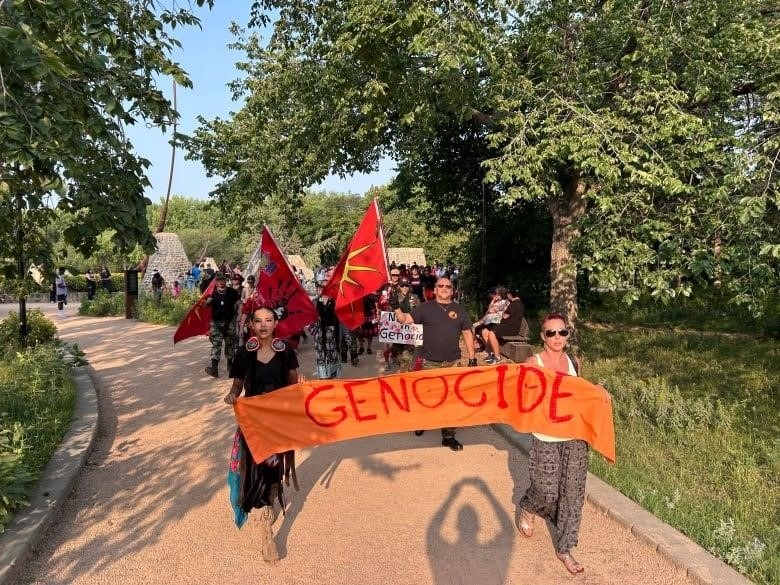 Photo shows people walking in a large line. In front are people holding a banner that says the word genocide in red letters. 
