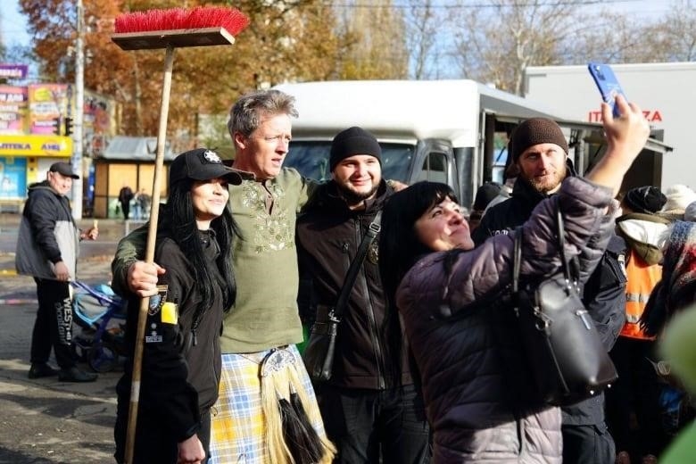 A man wearing a yellow and blue kilt takes a selfie with a group of people. 