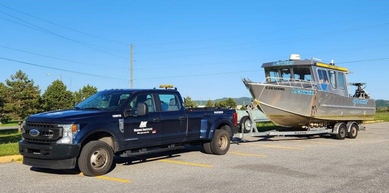 A pickup truck emblazoned with 'Marine Institute' is pictured towing the Cartwright, a small boat about the length of a car.