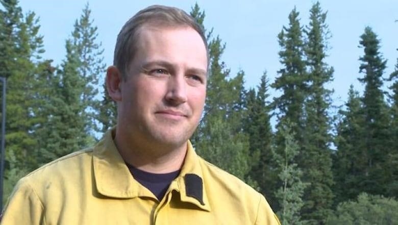 A man in a yellow shirt stands in a forest.