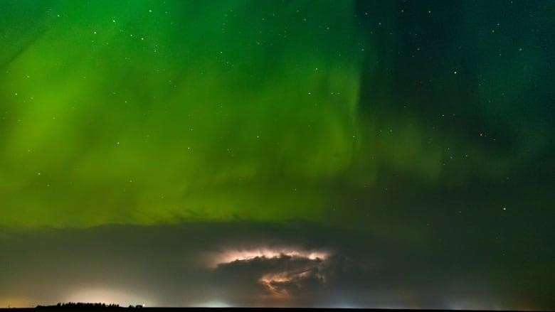 Stunning green northern lights can be seen in the sky along with some lightning underneath it. 