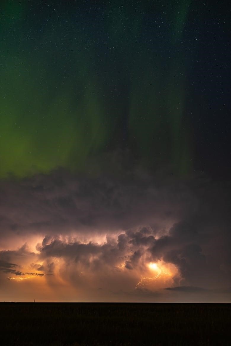 The beautiful sky can be seen with auroras in green and lightning and thunder beneath it along with some clouds. 
