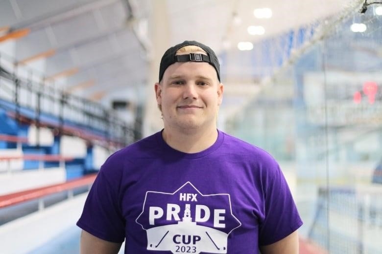 A person wearing an HFX Pride Cup t-shirt is standing in a hockey arena.