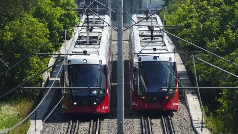 Two red and white light rail trains next to each other on the tracks.