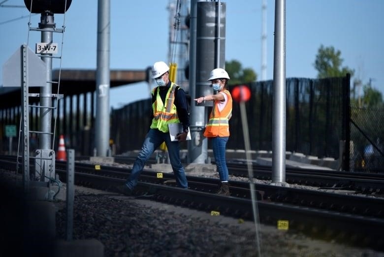 Two people in hihg-viz vests and hardhats inspect some railway tracks.