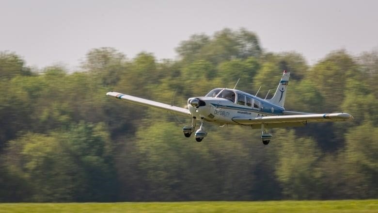 A small plane flies, with a motion blur on the trees in the background. 