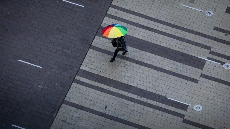 A person walks in the rain with an umbrella near the City Centre Library in Surrey, B.C., on Oct. 21, 2022. 
