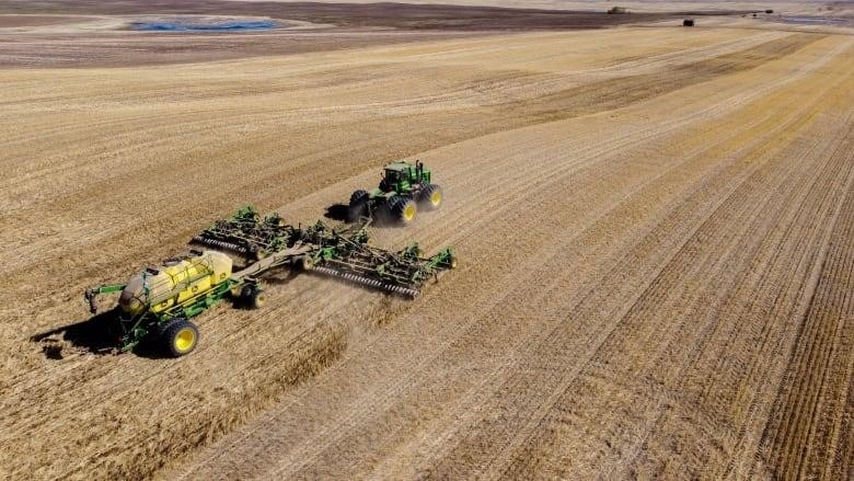 A green and yellow John Deere tractors is in a large brown farm field.