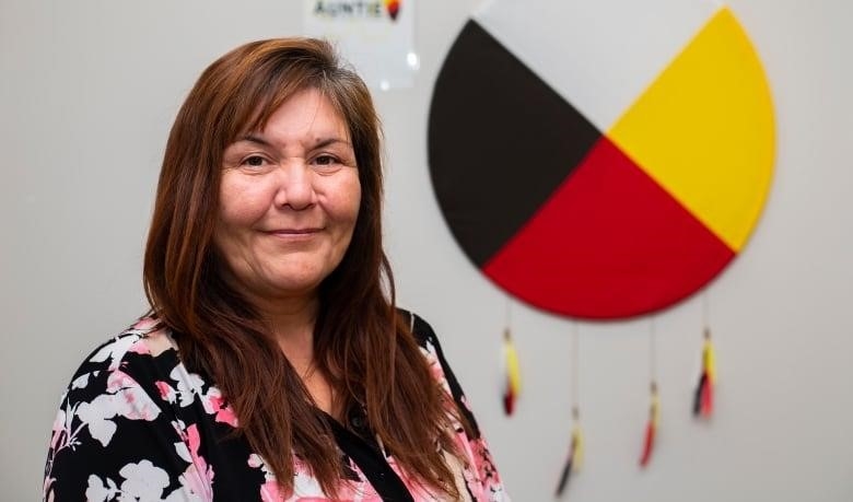 An older Indigenous women smiles standing in front of a medicine wheel.