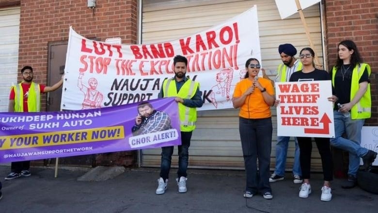 A person in orange top has the mic and is surrounded by people holding banners and placards. 