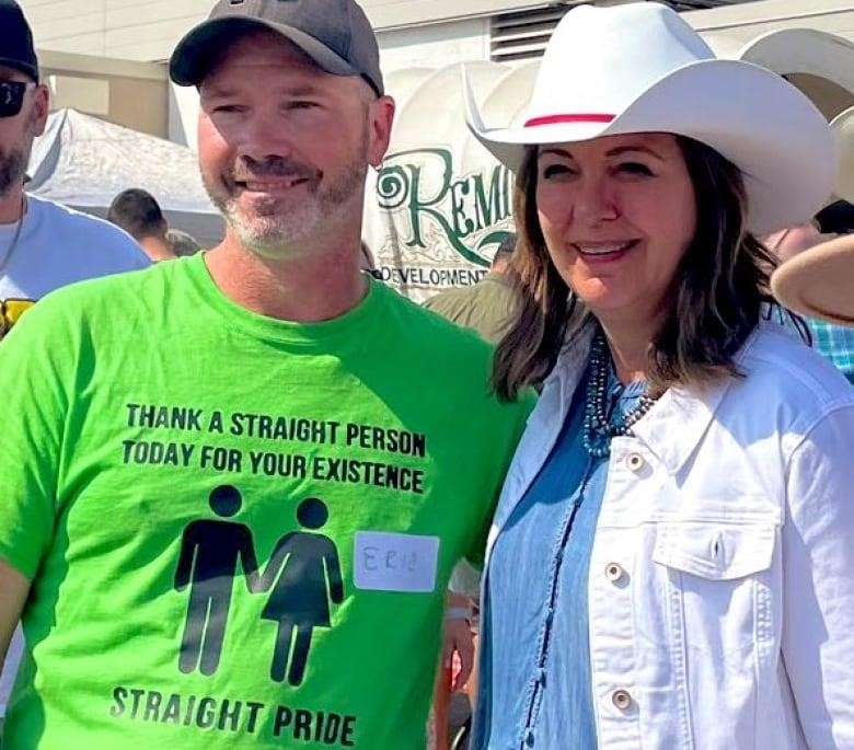 Man in provocative green shirt poses next to woman dressed in western gear.