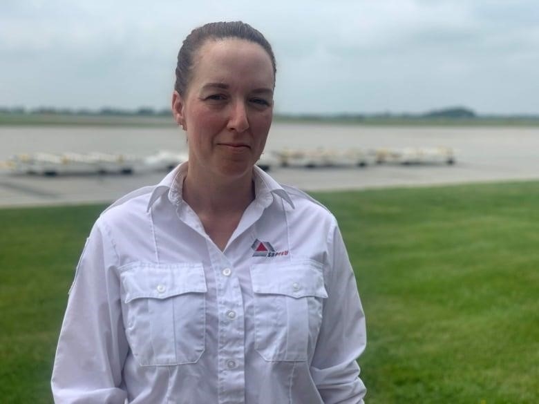 A woman stands outdoors at an airport on an overcast day.