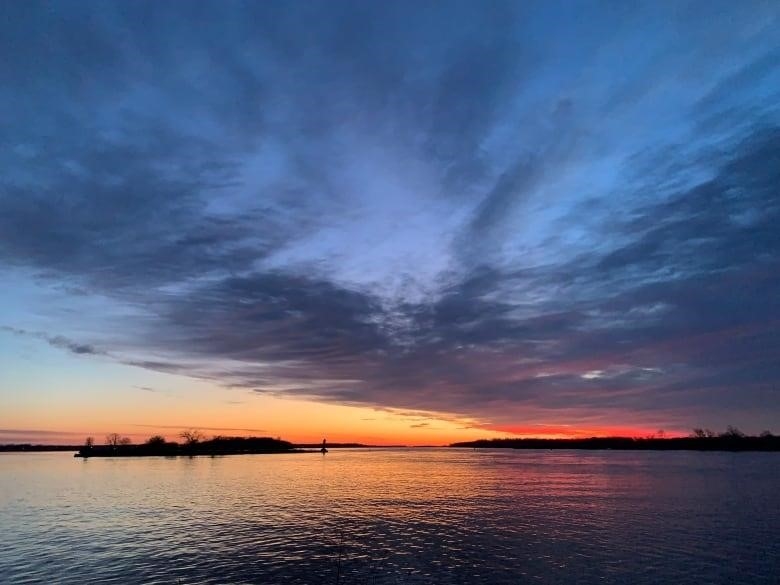 The sun rises over a river. 