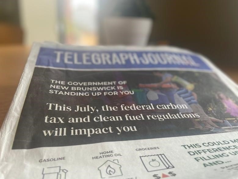 A newspaper titled "Telegraph Journal" with a front page ad that says "The Government of New Brunswick is standing up for you | This July, the federal carbon tax and clean fuel regulations will impact you"