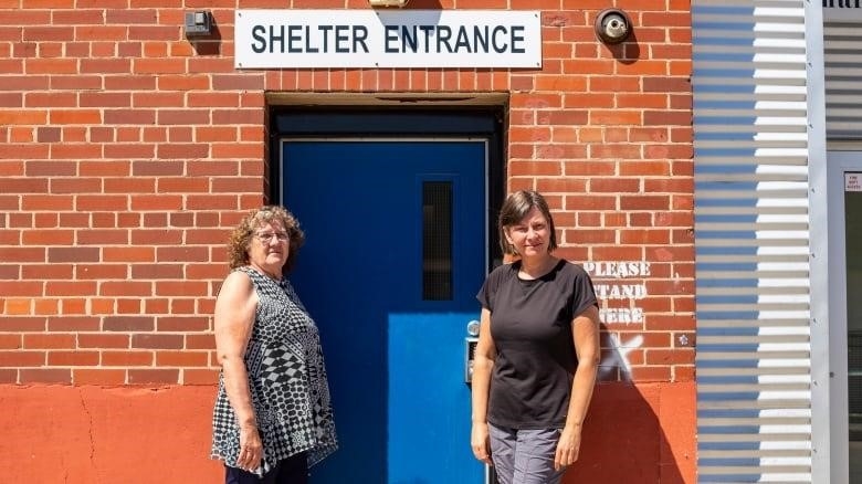 Two women stand by a blue door that leads to a homeless shelter.