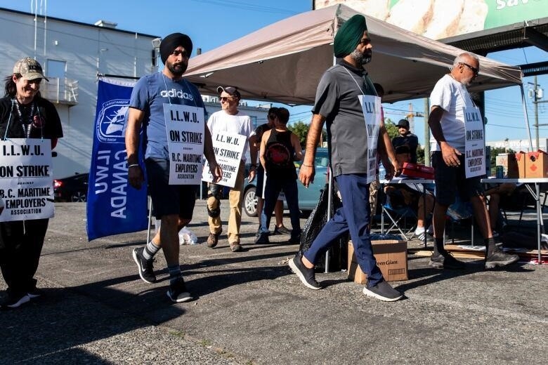Four men march around a tent bearing strike placards and carrying a dockworkers' union flag.