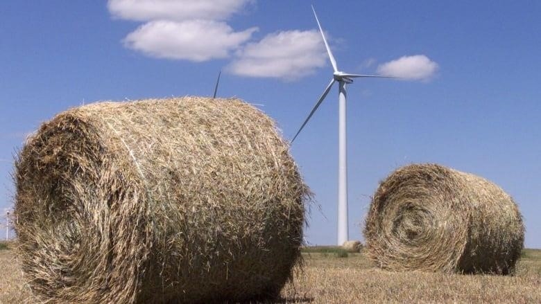 A wind turbine stands between two bales of hay