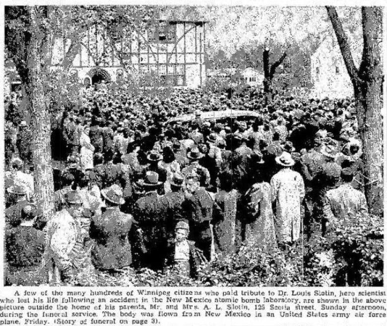 A black-and-white newspaper photo shows a crowd filling a street outside of a home.