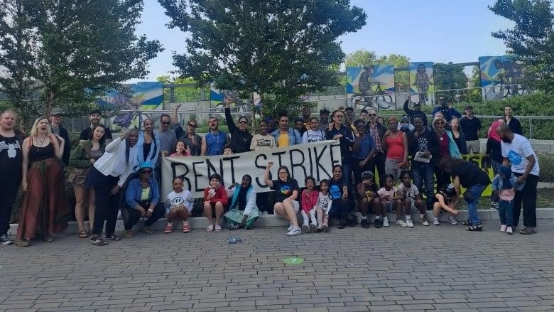 A crowd of people pose for a picture around a sign that says "RENT STRIKE".