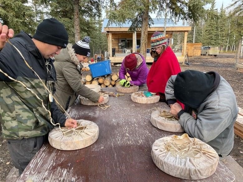 A group of people work at a table outside, making drums.