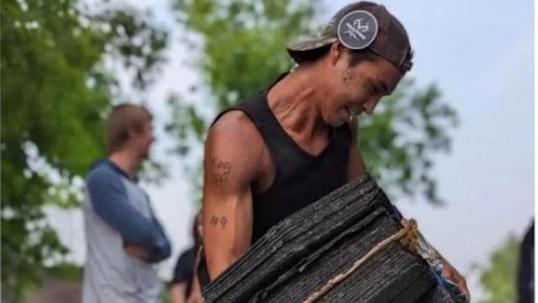 A man holds a stack of roof shingles 