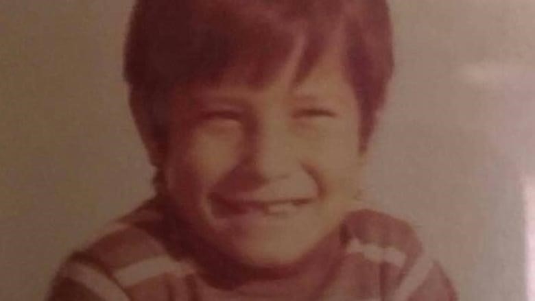 A grainy, sepia-tinted image of a little boy with short brown hair, wearing a striped shirt, smiling into the camera.