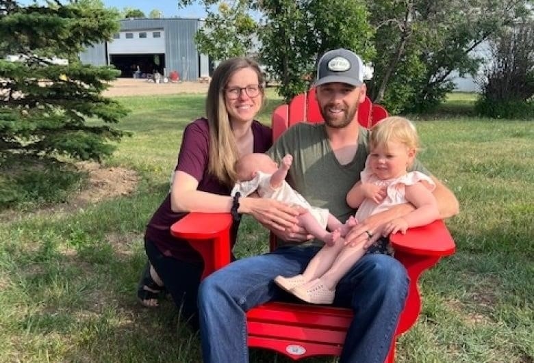 A man sits in a chair holding two young children, with a woman crouched next to him.