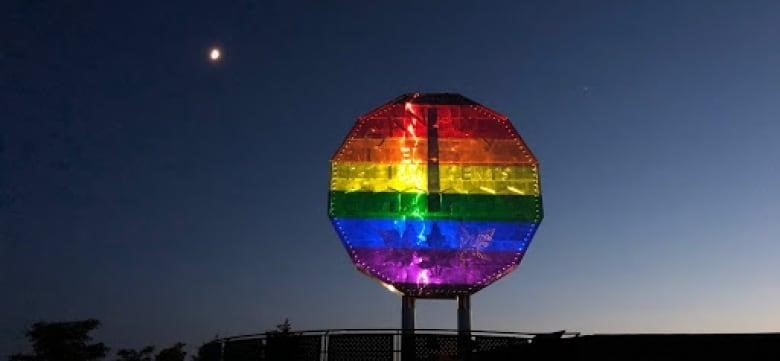 A colourful giant nickel statue is illuminated at night with the moon in the background.