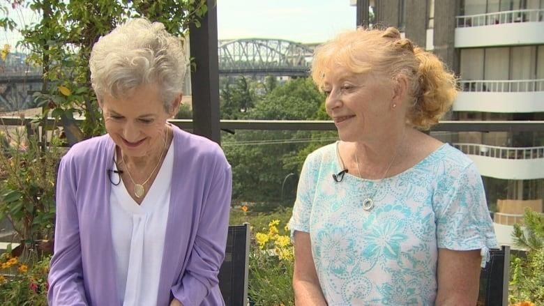 Two women point to awards and news clippings on a wall.