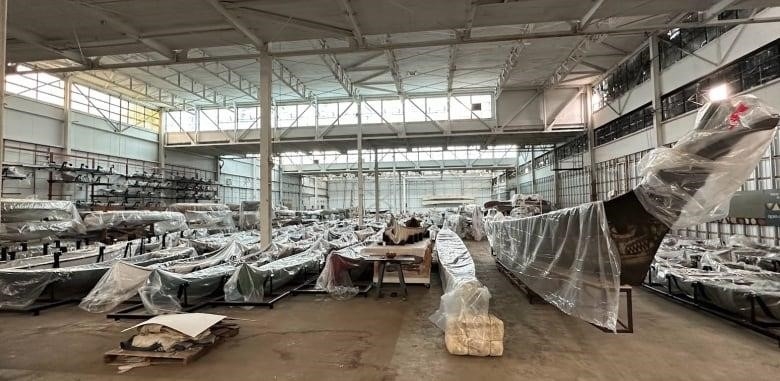 Rows of canoes and kayaks under plastic sheeting in a warehouse building. 