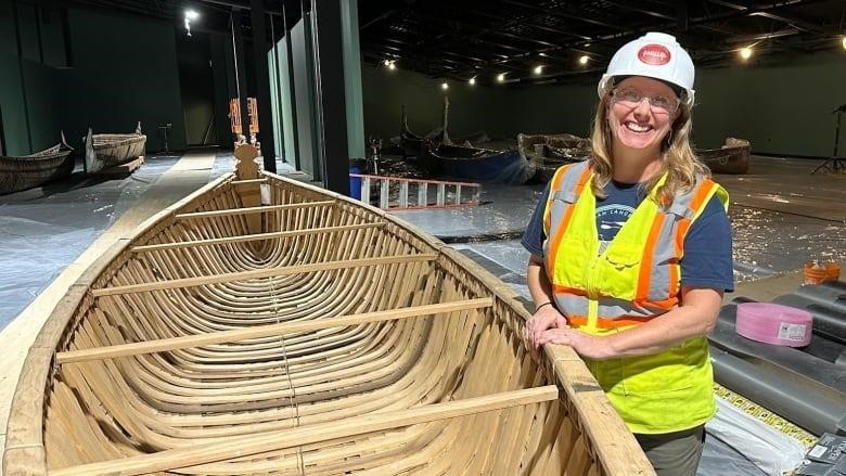 Portrait of Carolyn Hyslop, wearing a hardhat and safety goggles, standing beside a birchbark canoe. 