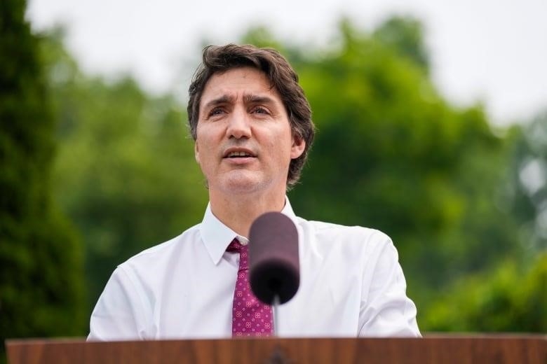 Prime Minister Justin Trudeau makes an announcement in a white shirt and red tie while outside. 