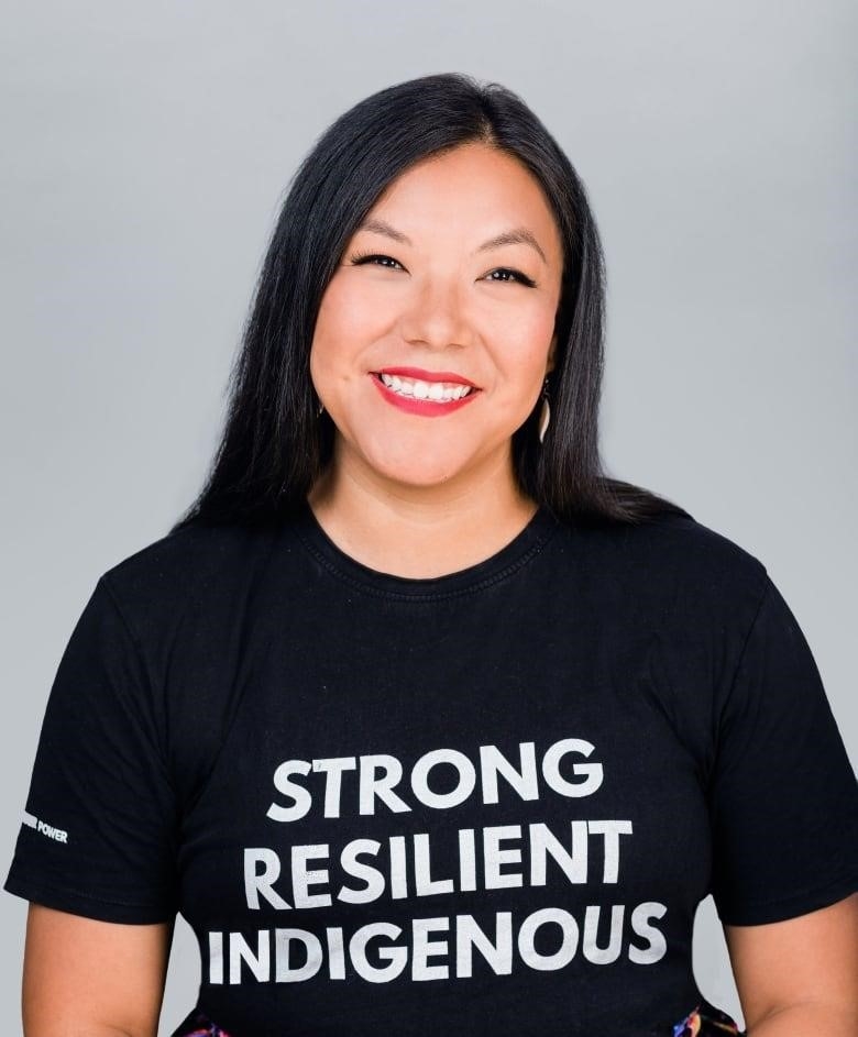 An Anishinaabe woman in a black t-shirt that reads Strong, Resilient, Indigenous, smiles at the camera.